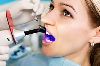The image shows a woman receiving dental treatment, with a dental professional using an electric toothbrush to clean her teeth.