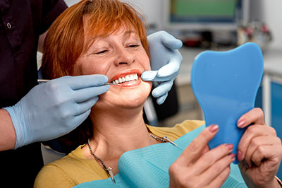 Woman in dental chair with blue mouthguard, smiling at camera, receiving dental treatment.