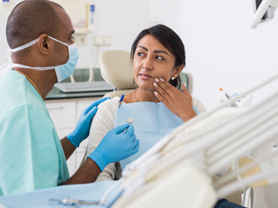 A dental professional is assisting a patient in a dental chair, with the professional wearing gloves and a face mask.