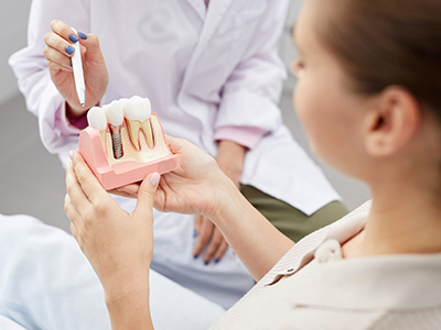An image featuring a dental professional holding a pink model of a mouth with teeth, while a patient observes the demonstration.