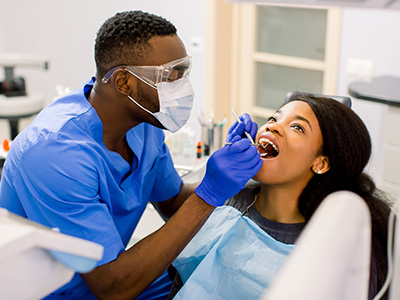 The image shows a dental professional performing oral care on a patient, with the professional wearing protective gear and using dental instruments.