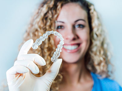 An individual, possibly a woman, is holding up a clear dental retainer with both hands against a white background.