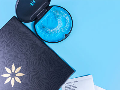A blue case holding a toothbrush with bristles, placed next to an open book or brochure with a floral design.