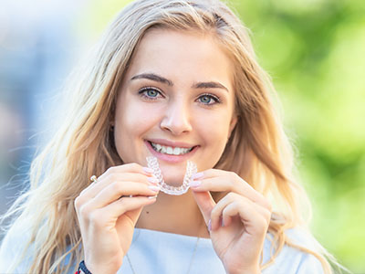 A smiling woman holding a toothbrush in her mouth.