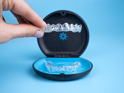 The image shows a person s hand holding an open box containing a set of clear, acrylic dental retainers or aligners.