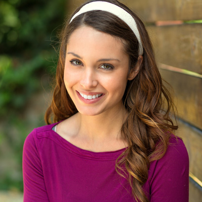 A young woman with long hair, wearing a purple top and headband, smiling at the camera.