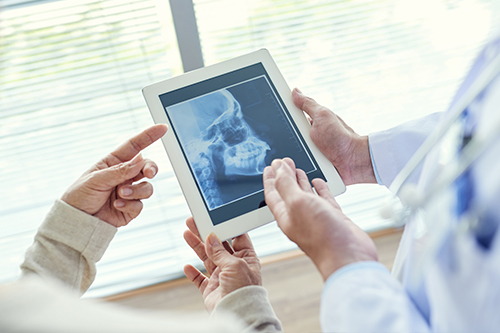 A healthcare professional holding a tablet with an X-ray image displayed, showing the X-ray to two people.