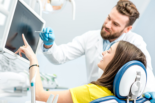 A dental professional is assisting a patient with a digital display, both in a modern dental office setting.